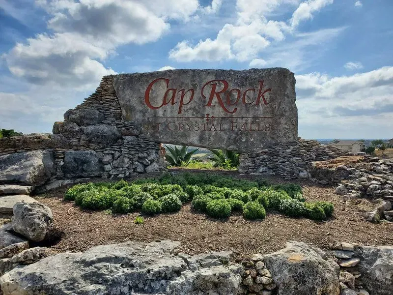 A large stone sign that says cap rock is surrounded by rocks.