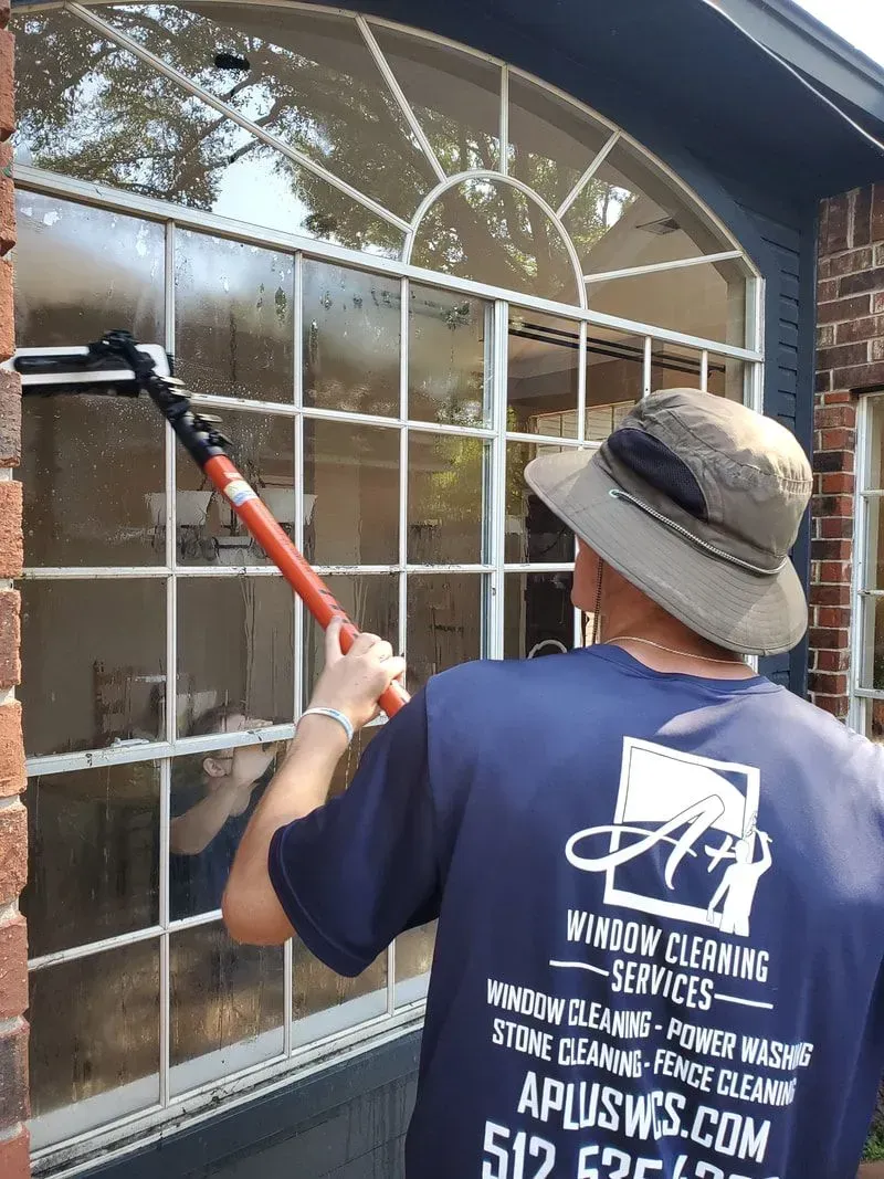 A man wearing a hat is cleaning a window with a brush.