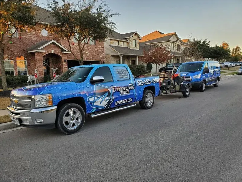 Two blue trucks are parked on the side of the road next to a house.