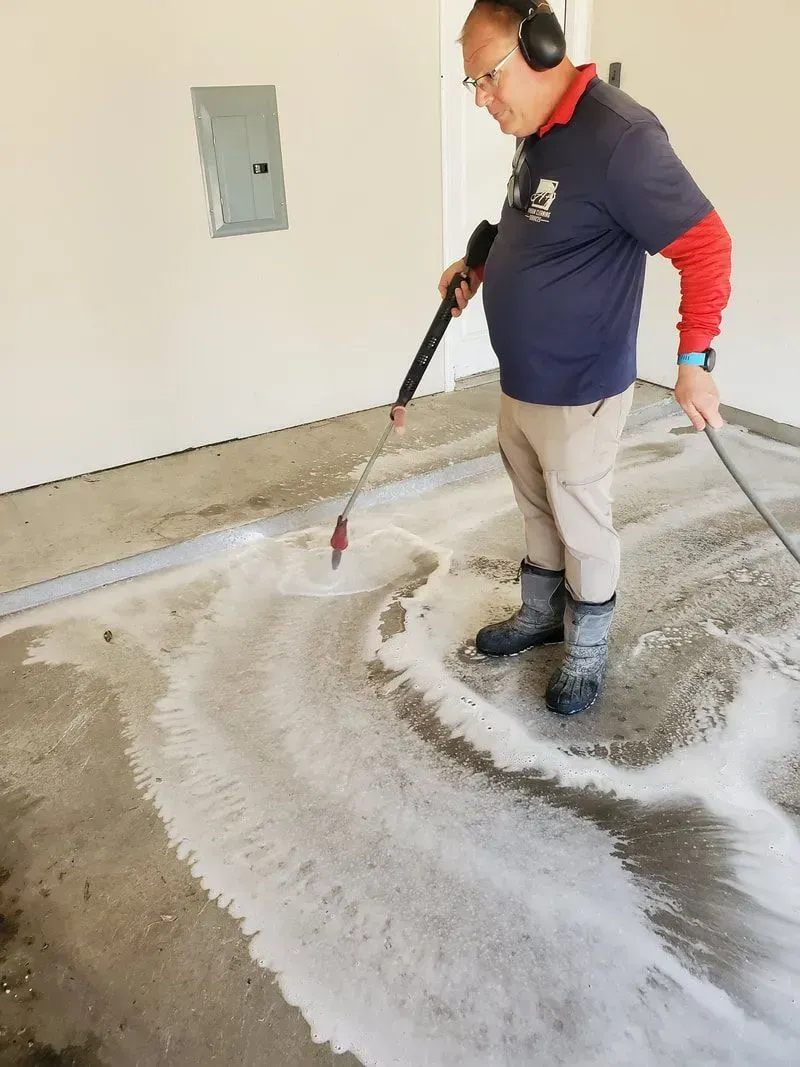 A man is using a high pressure washer to clean a garage floor.