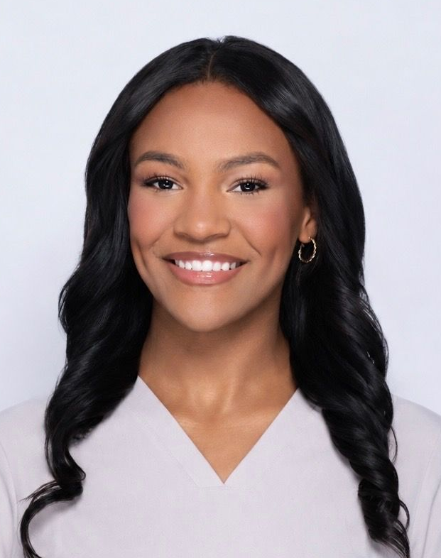 Headshot of a smiling woman with long black hair wearing a white top against a light background with clear skin