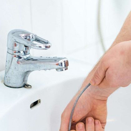 A person is holding a hose in their hand in front of a sink.
