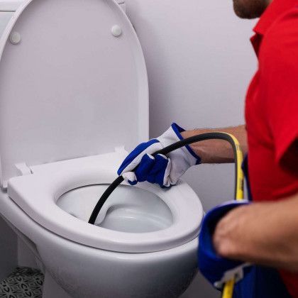 A man is cleaning a toilet with a hose.