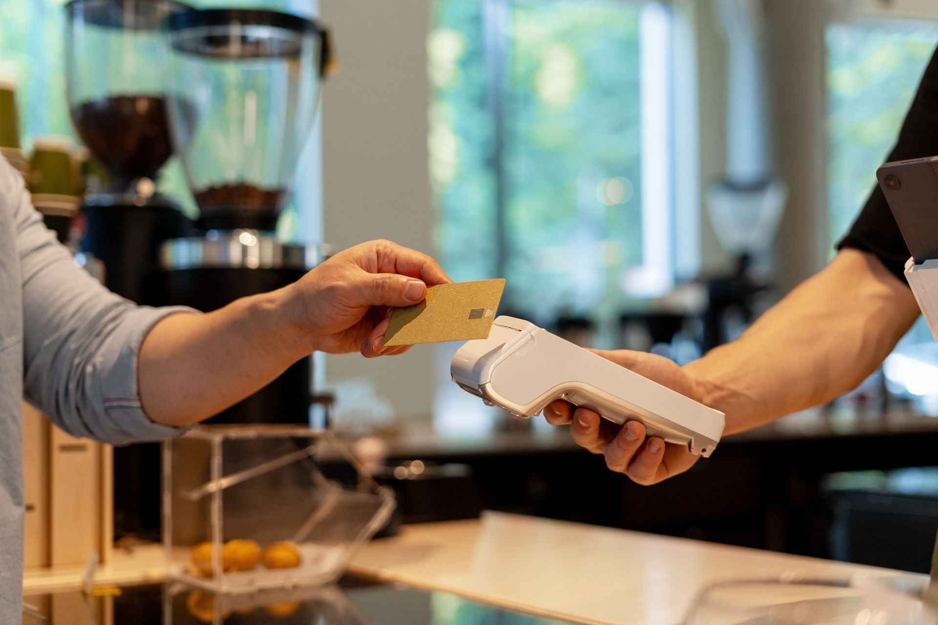 Person paying with a card at a cafe counter, tapping the card on a card reader. Person paying with a card at a cafe counter, tapping the card on a card reader.