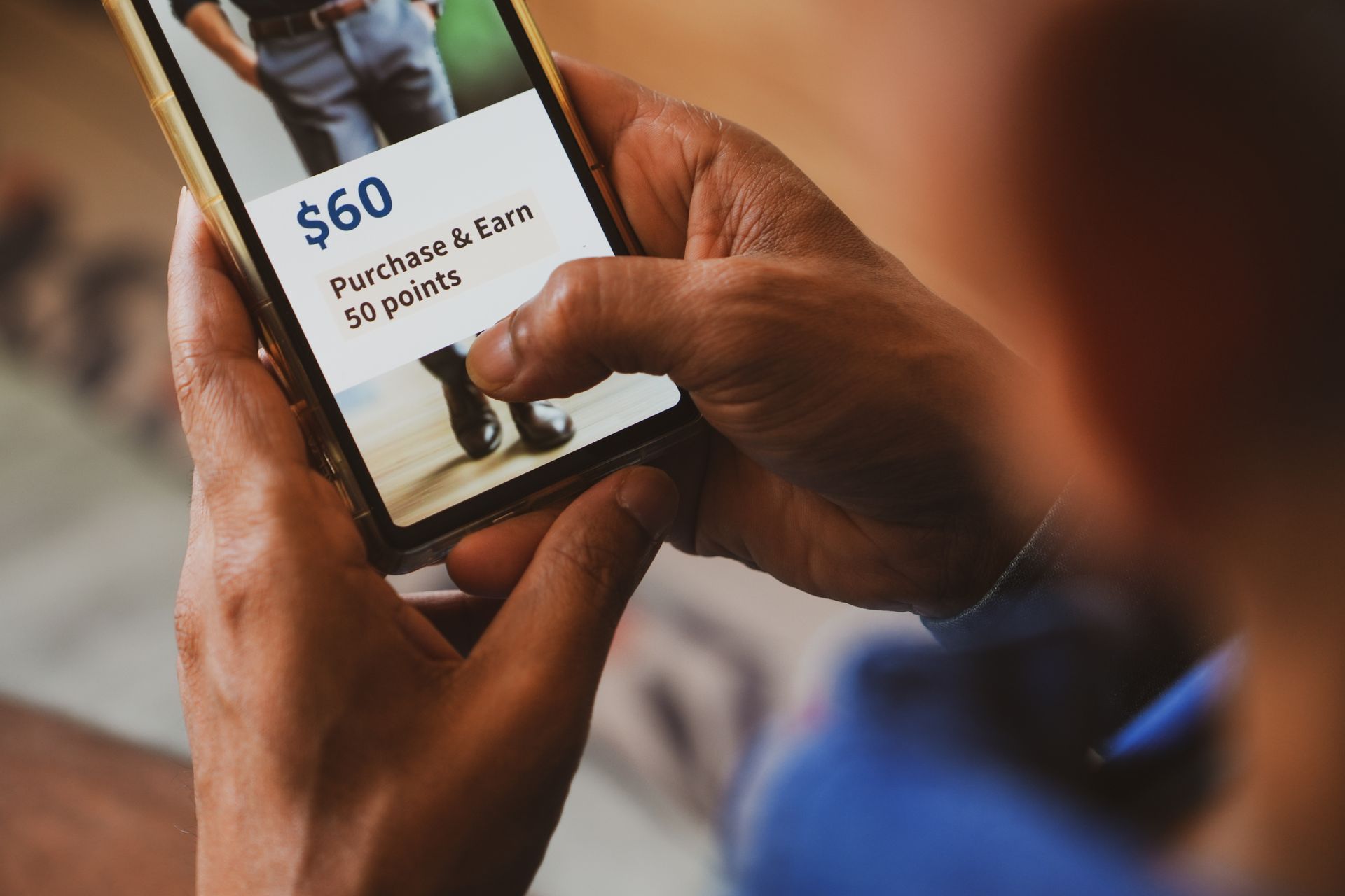 Person holding a phone displaying a shopping rewards offer: spend $60, earn 50 points. Person holding a phone displaying a shopping rewards offer: spend $60, earn 50 points.