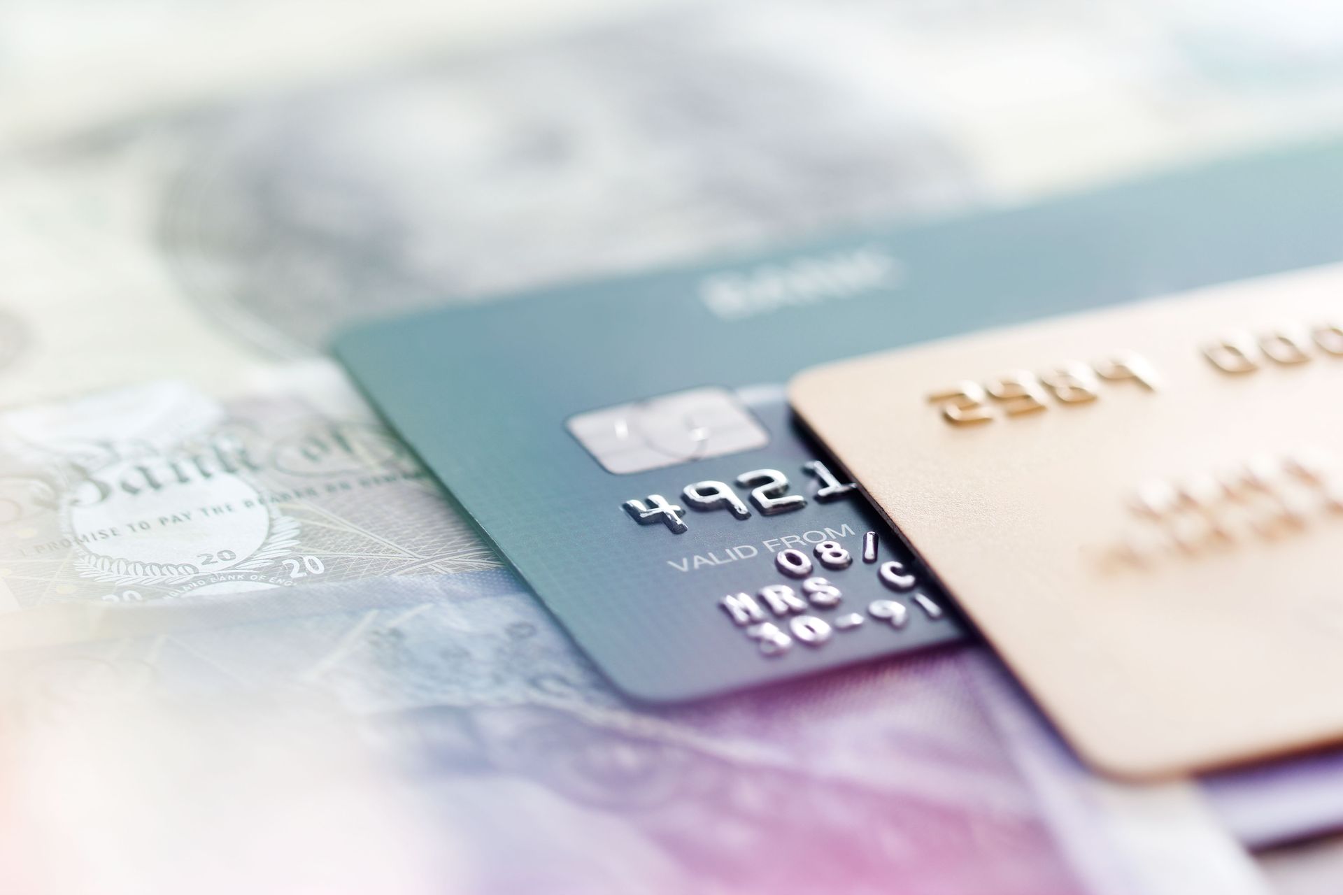 Two credit cards, teal and gold, on a blurred background of currency. Two credit cards, teal and gold, on a blurred background of currency.