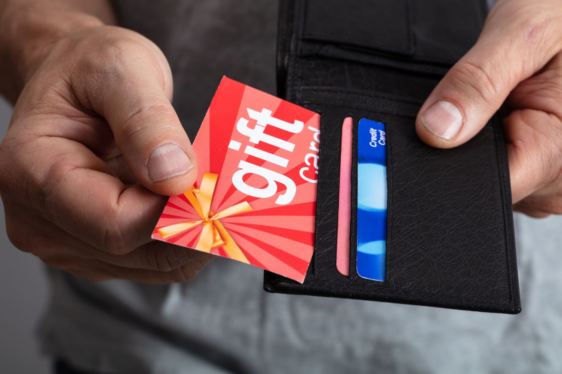 Person holding a black wallet, removing a red and white gift card. Person holding a black wallet, removing a red and white gift card.