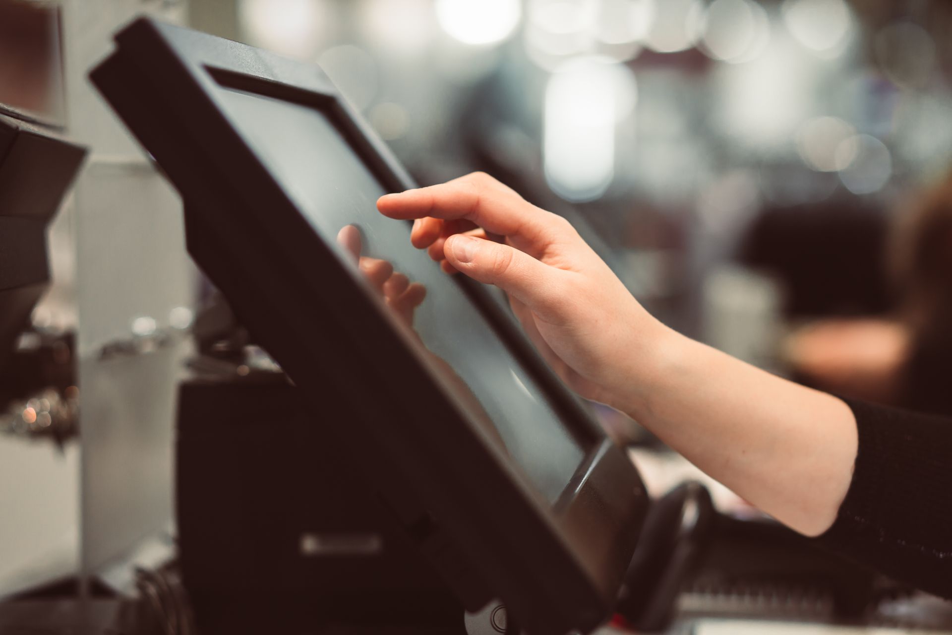 A hand touches a touchscreen point-of-sale system in a retail setting. A hand touches a touchscreen point-of-sale system in a retail setting.