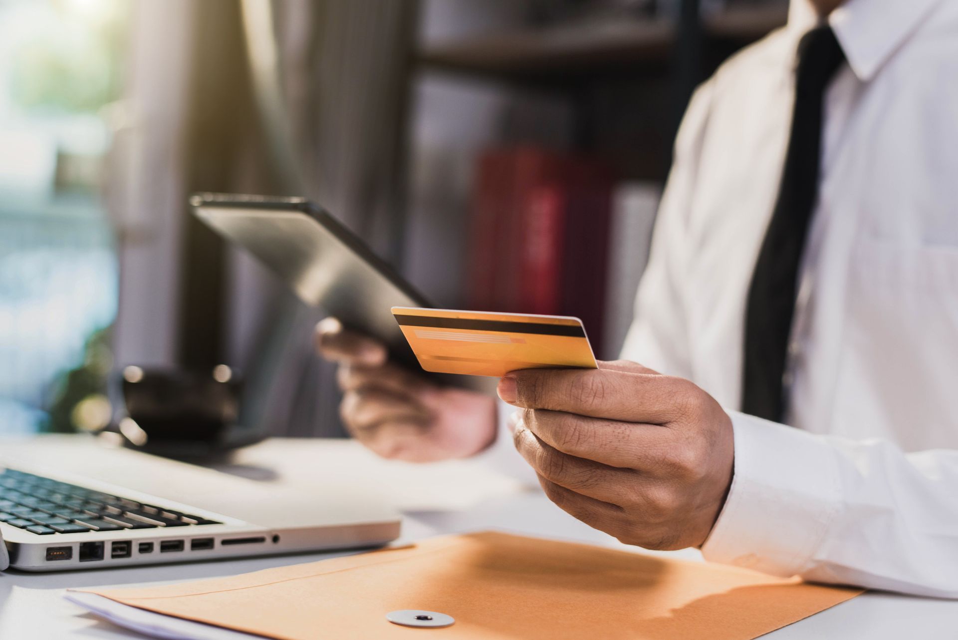 Person in office attire holding a credit card and tablet next to a laptop. Person in office attire holding a credit card and tablet next to a laptop.
