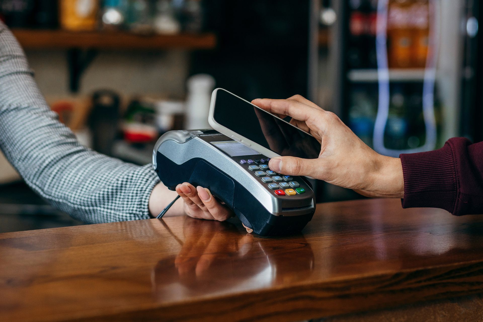 Person using smartphone to pay at a point-of-sale terminal on a wooden counter. Person using smartphone to pay at a point-of-sale terminal on a wooden counter.