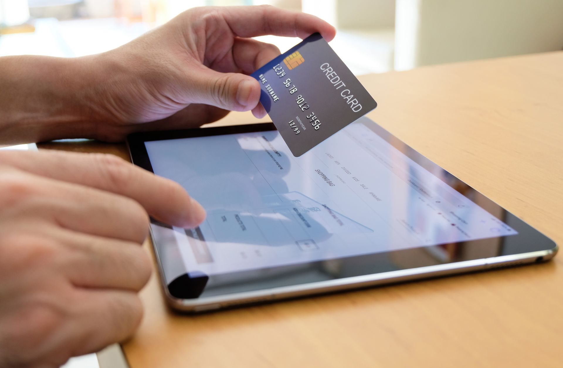 Person holding credit card over tablet, completing online purchase. Person holding credit card over tablet, completing online purchase.