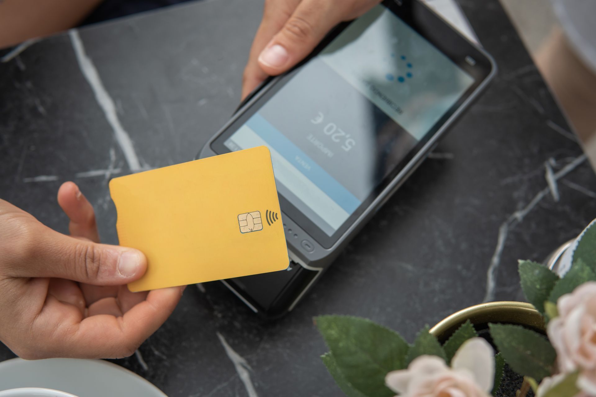 Person holding a yellow card near a payment terminal on a black and white marble table. Person holding a yellow card near a payment terminal on a black and white marble table.
