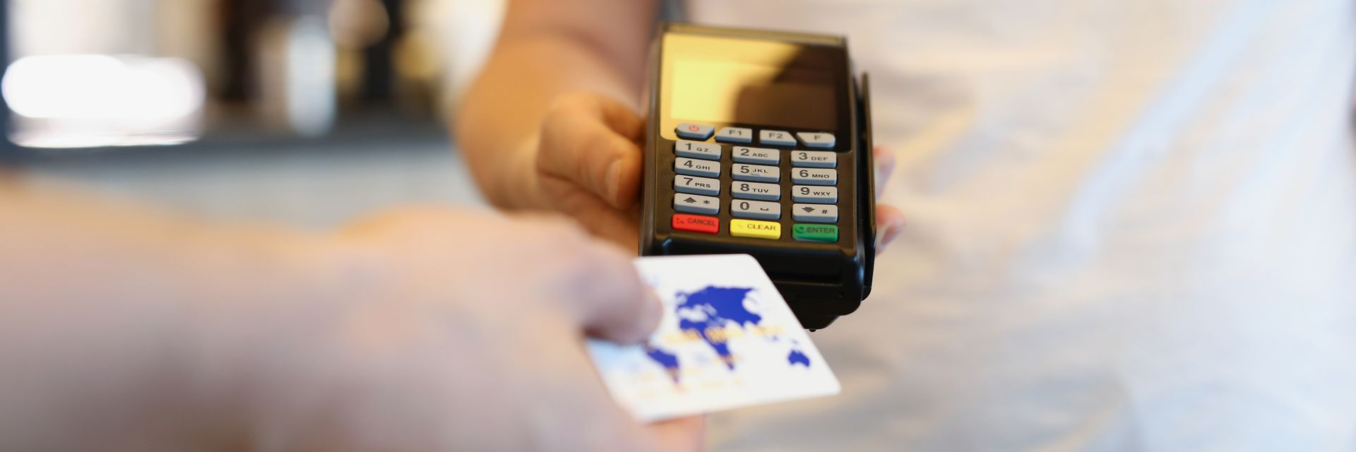 Hand holding a credit card over a point-of-sale device. The card has a world map design. Hand holding a credit card over a point-of-sale device. The card has a world map design.
