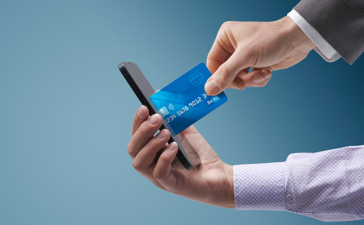 Hand holding a blue credit card near a smartphone, possibly for payment. Hand holding a blue credit card near a smartphone, possibly for payment.