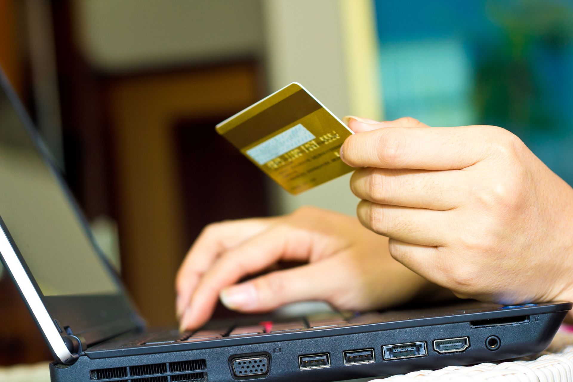 Person using a laptop with one hand holding a gold credit card while typing. Person using a laptop with one hand holding a gold credit card while typing.