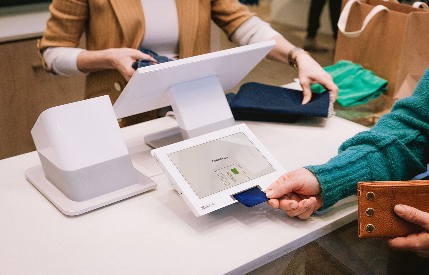 Customer swipes card at a point-of-sale system in a retail store. Shop assistant handles folded garments. Customer swipes card at a point-of-sale system in a retail store. Shop assistant handles folded garments.