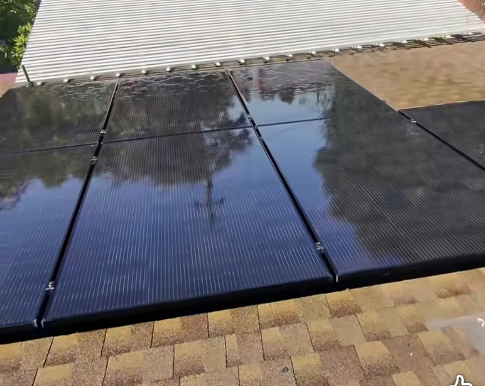 Clean rooftop solar panels reflecting trees and the neighboring roof.