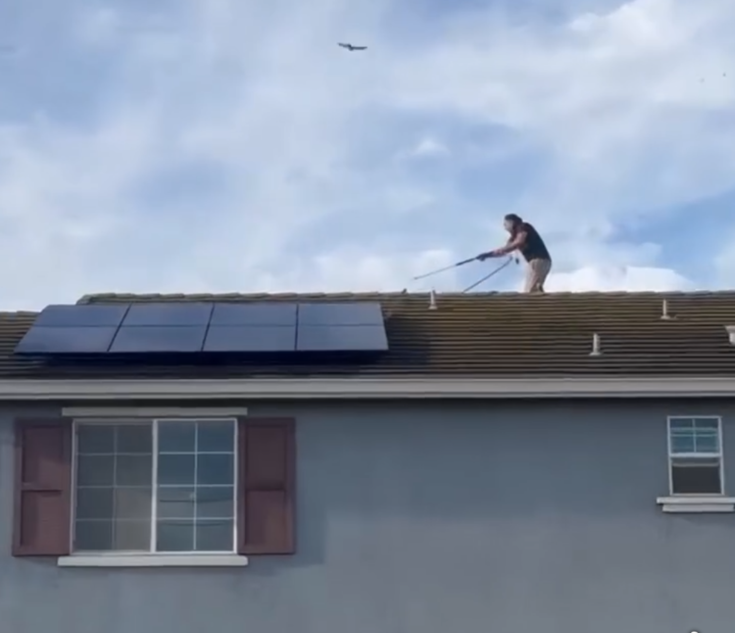Technician using an extended cleaning pole to wash solar panels on a Pittsburg home.
