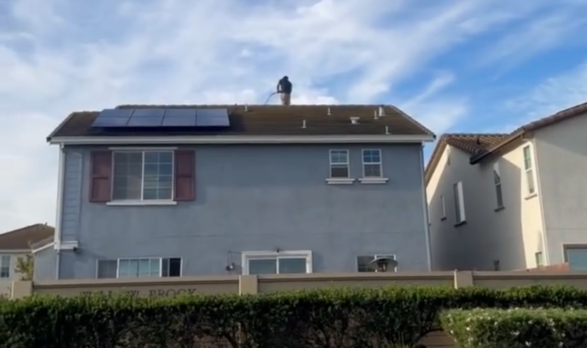 Rooftop solar panels on a two-story home with a technician near the roof ridge.