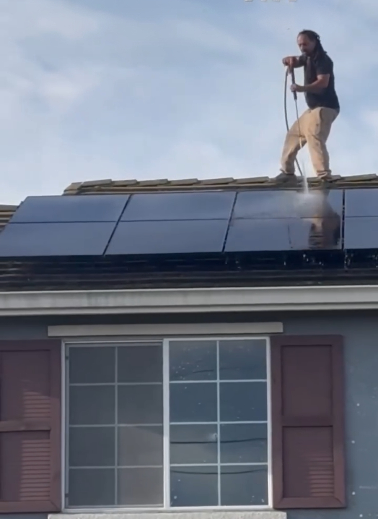 Technician using a long cleaning pole to wash rooftop solar panels in Pittsburg.