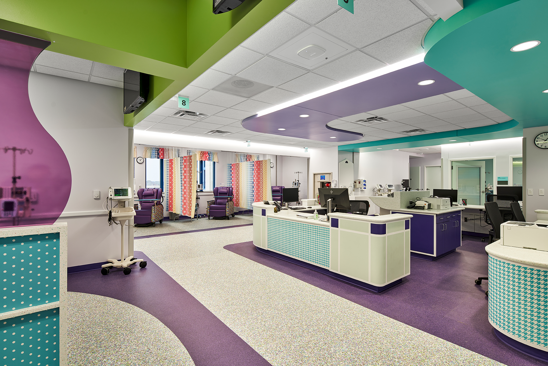 Interior view of a colorful children's hospital room with medical equipment, workstations, and vibrant purple, green, and teal accents.