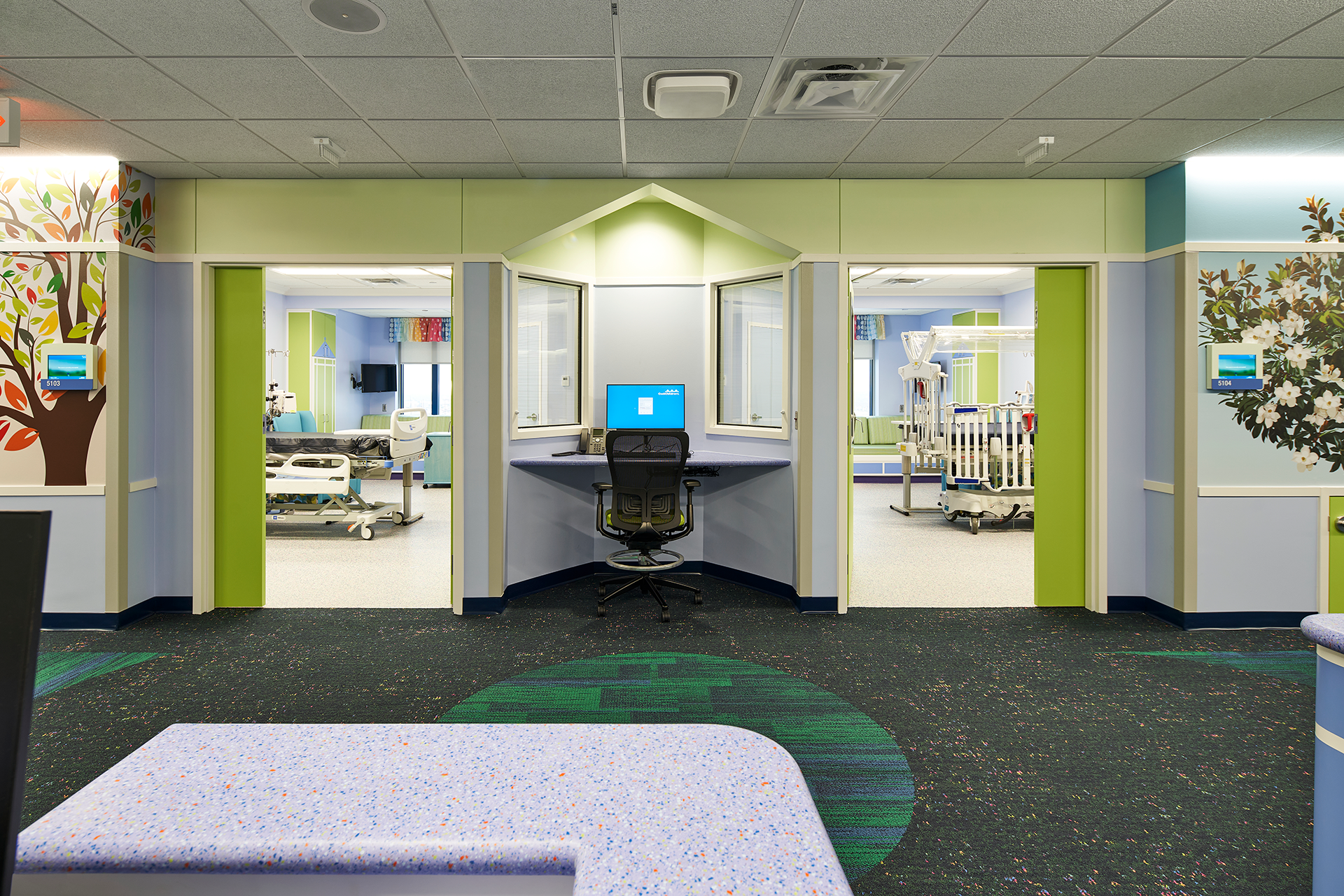 View of a brightly colored children's hospital room with an angled nurse's station between two patient rooms.