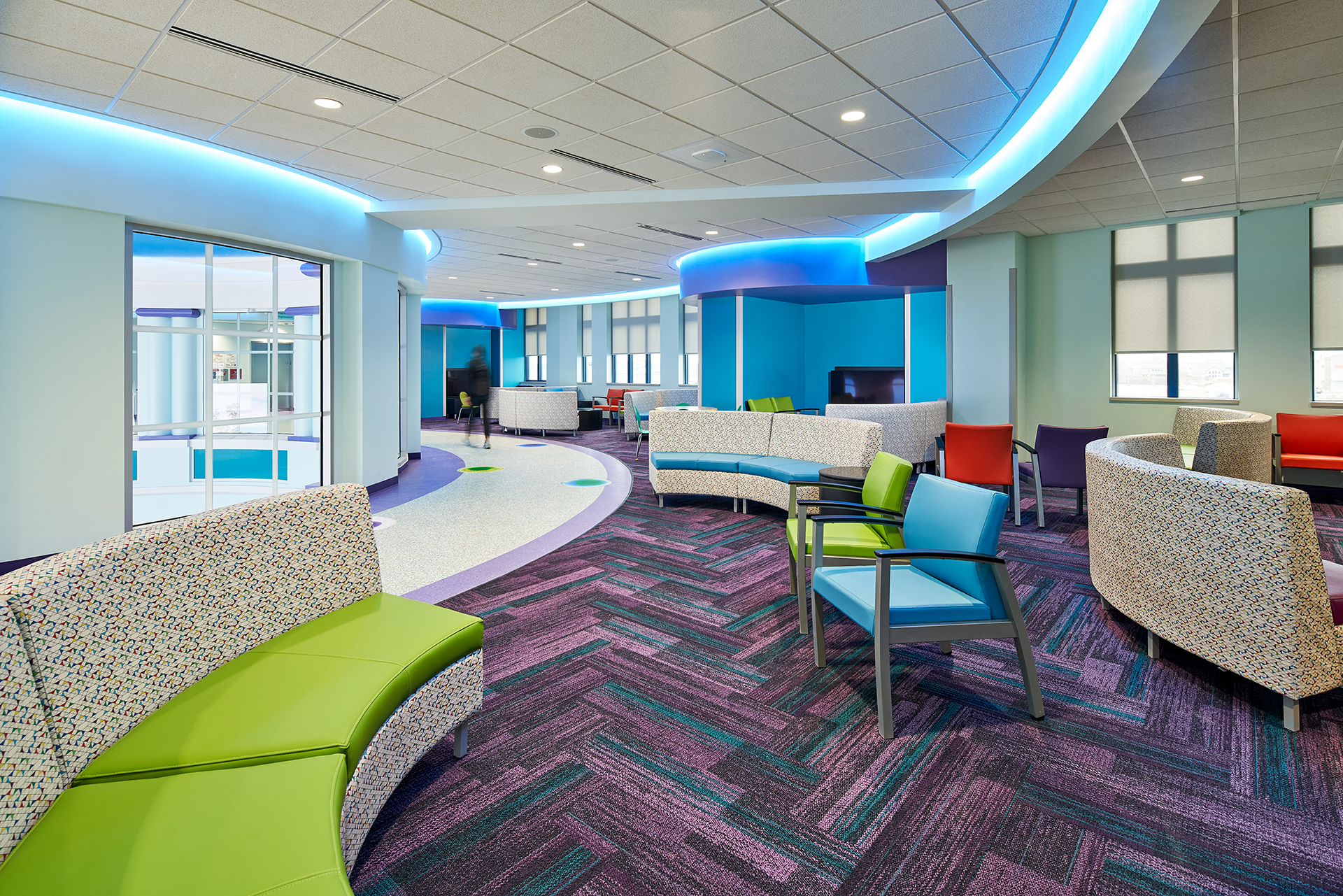 Brightly colored waiting room with curved seating, patterned carpet, and blue accent lighting.
