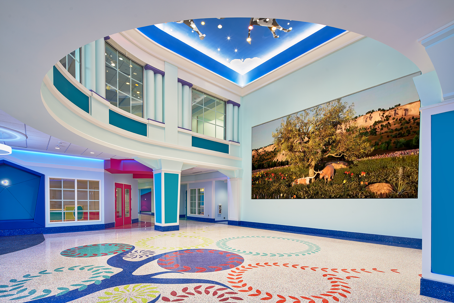 A colorful lobby with mosaic floor art and a large screen displaying an outdoor scene. Blue, white, and other bright colors are used throughout.