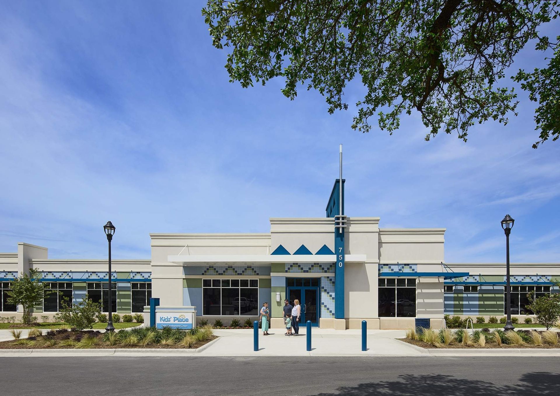 Modern white building with blue accents and a central entrance, viewed from a sidewalk under a clear sky