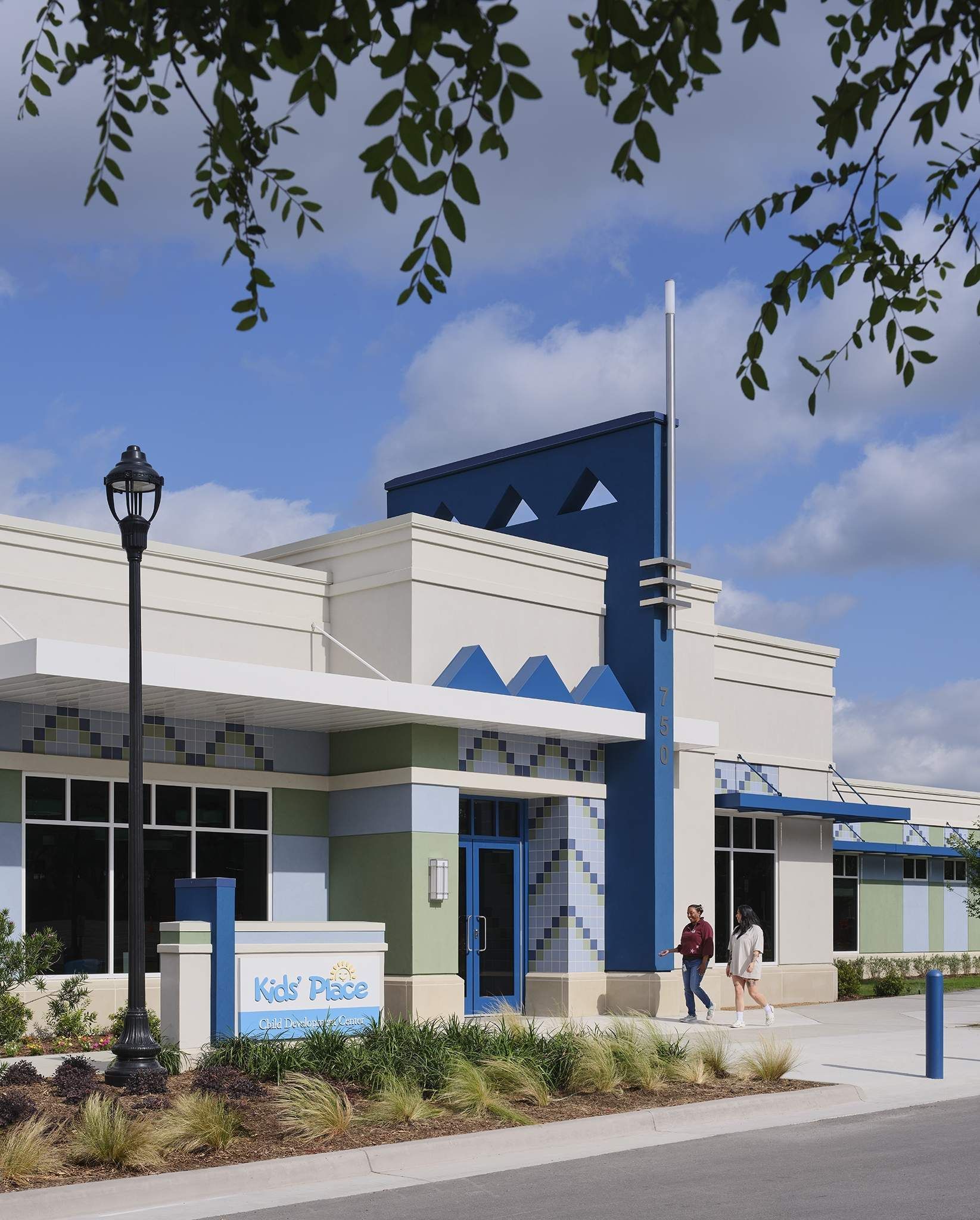 Modern blue-and-white building exterior with a walkway, lamp post, and a person near the entrance