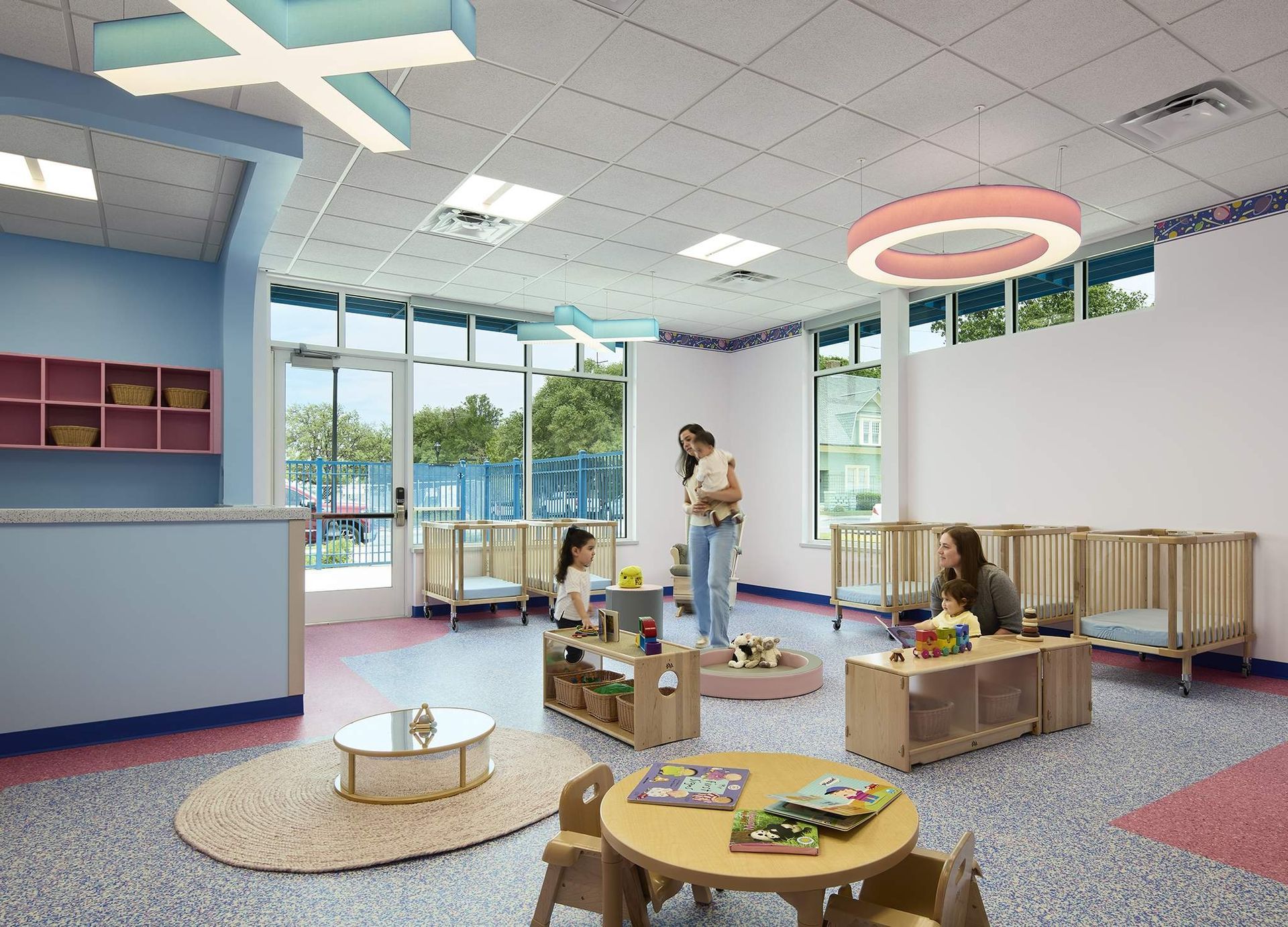 Bright preschool classroom with a teacher and children playing on colorful rugs and tables