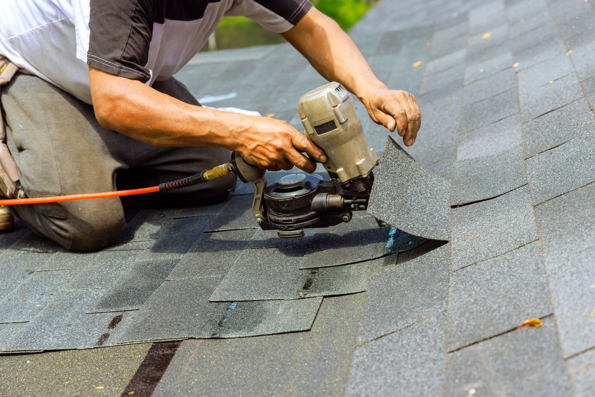 Close-up of a residential roof repair contractor using a pneumatic air nail gun on a shingles roof.