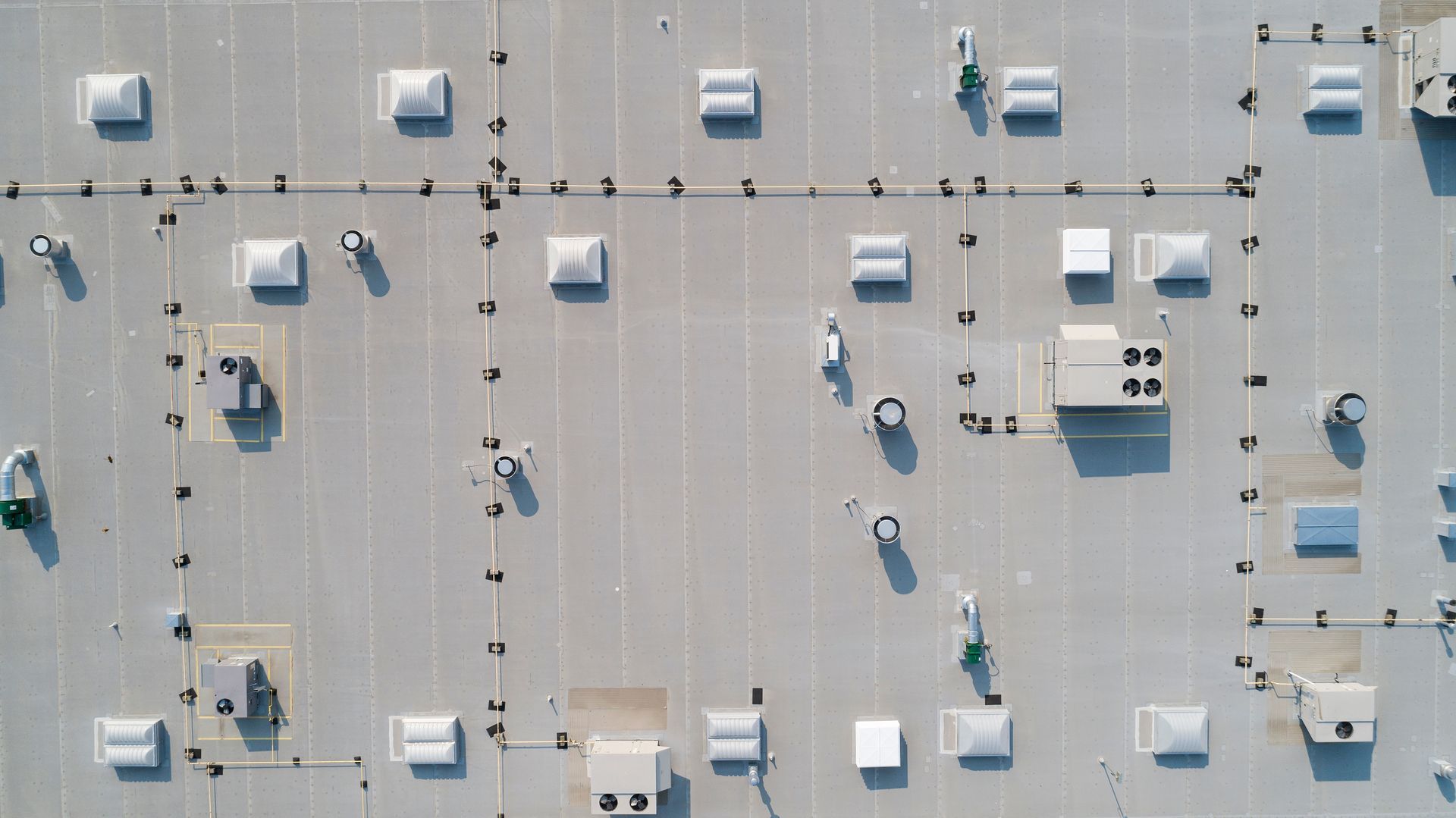 A professional performing a commercial roofing installation on a metal roof at sunset. Aerial view of a flat rooftop with HVAC units, vents, and scattered maintenance workers.