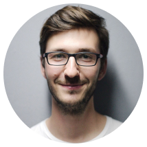 Man with glasses smiling, short brown hair, light stubble, against a gray backdrop.