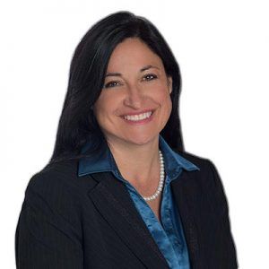 Woman with long black hair, wearing a black suit jacket over a blue shirt, smiling, and wearing a pearl necklace.