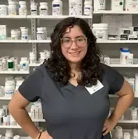 A woman is standing in front of a pharmacy shelf with her hands on her hips.