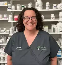 A woman wearing glasses is smiling in front of a pharmacy.