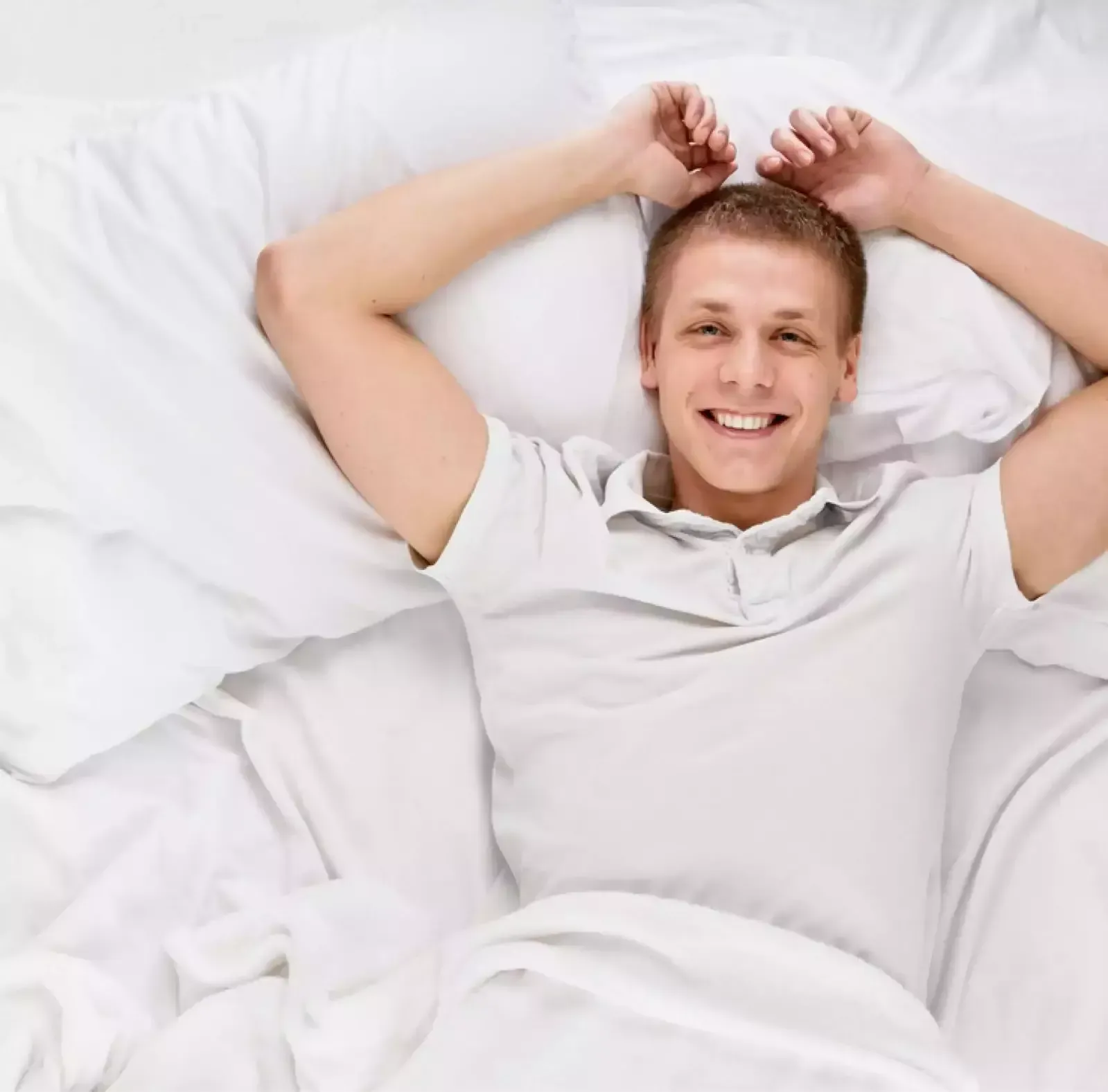 A man is laying in bed with his arms outstretched and smiling