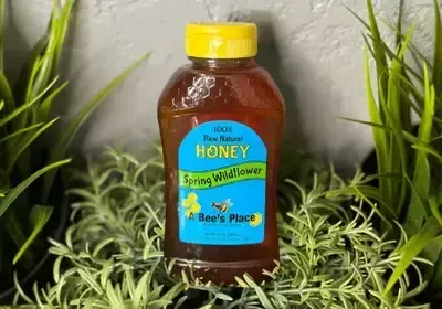 A bottle of honey is sitting on top of a lush green plant.