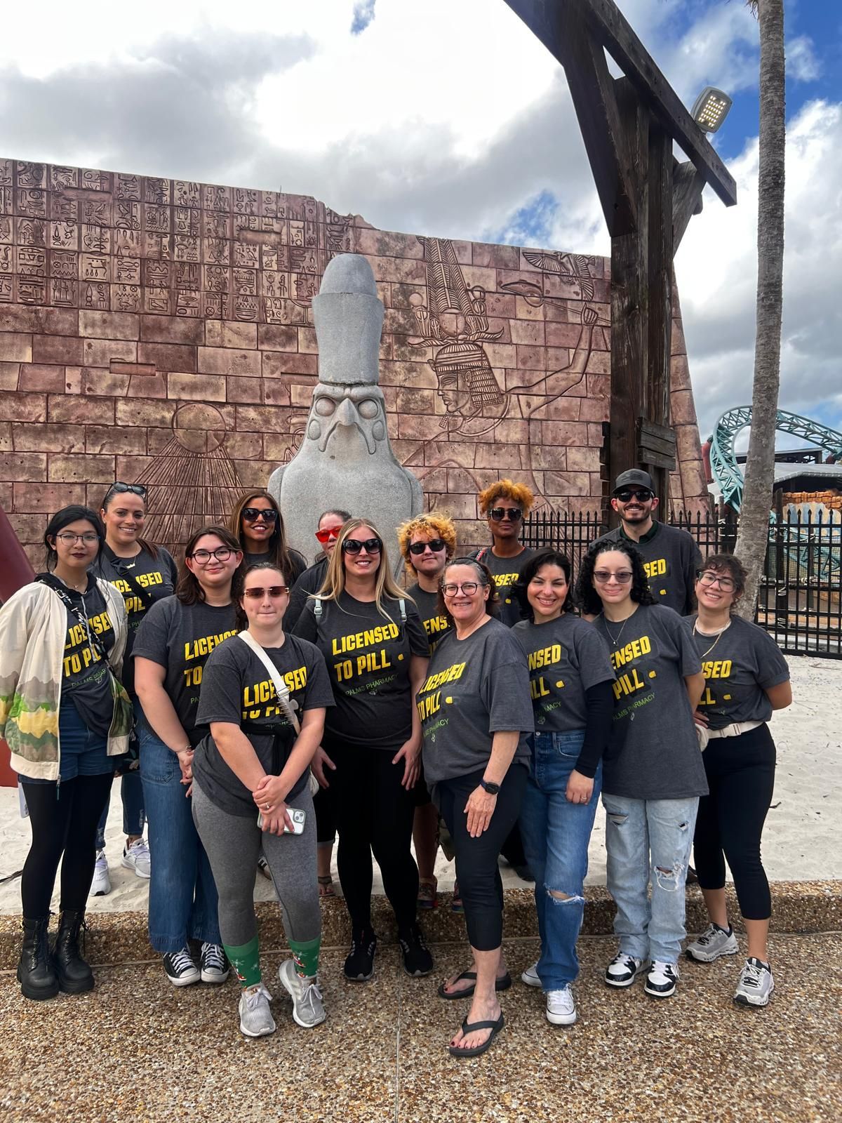 Group of people in matching t-shirts, posing in front of a stone wizard statue and a themed background.