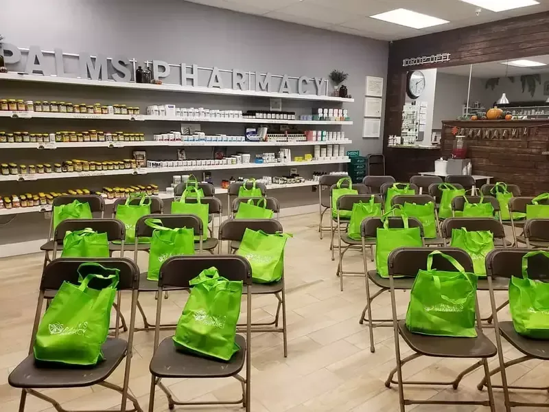 A row of folding chairs filled with green bags in a pharmacy.
