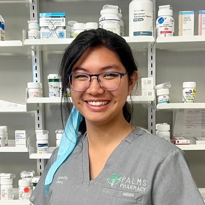 A woman in a blue scrub is standing in front of a pharmacy.