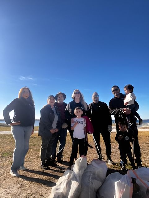 Group of people outdoors on a sunny day, standing in front of water. Holding bags of trash.