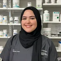 A woman wearing a hijab is standing in front of a pharmacy.