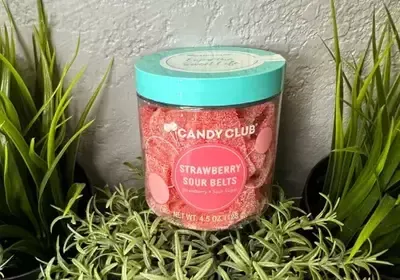A jar of candy club strawberry sour belts is sitting on top of a plant.