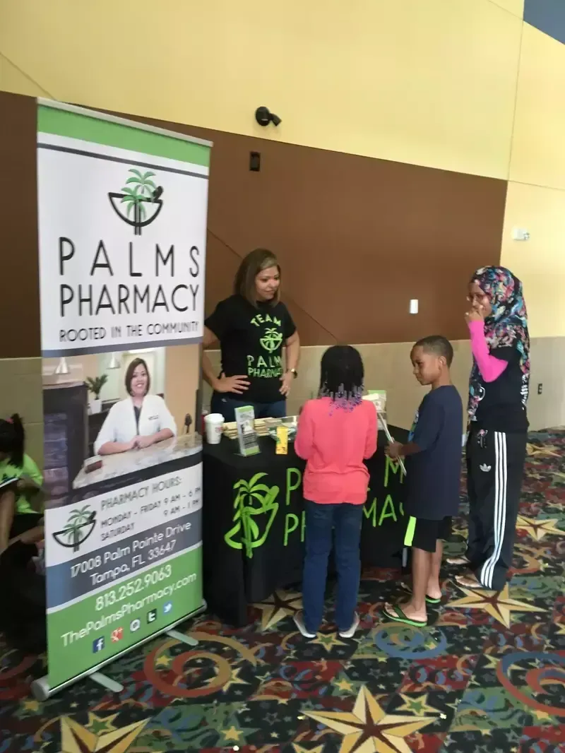 A group of people are standing around a table in front of a palms pharmacy sign.