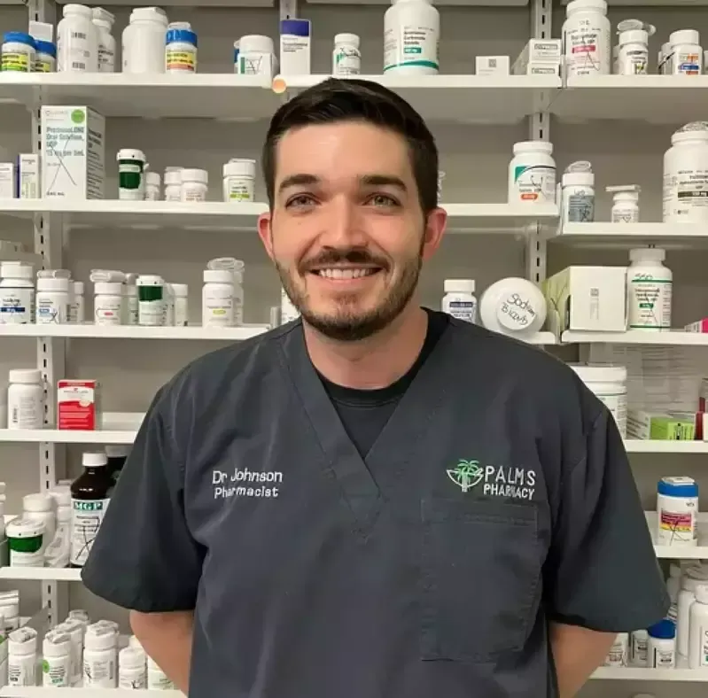 A man in a pharmacy is smiling in front of shelves full of pills