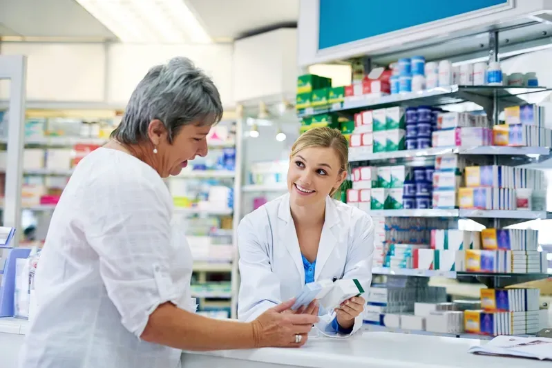 A female pharmacist is talking to an older woman in a pharmacy.