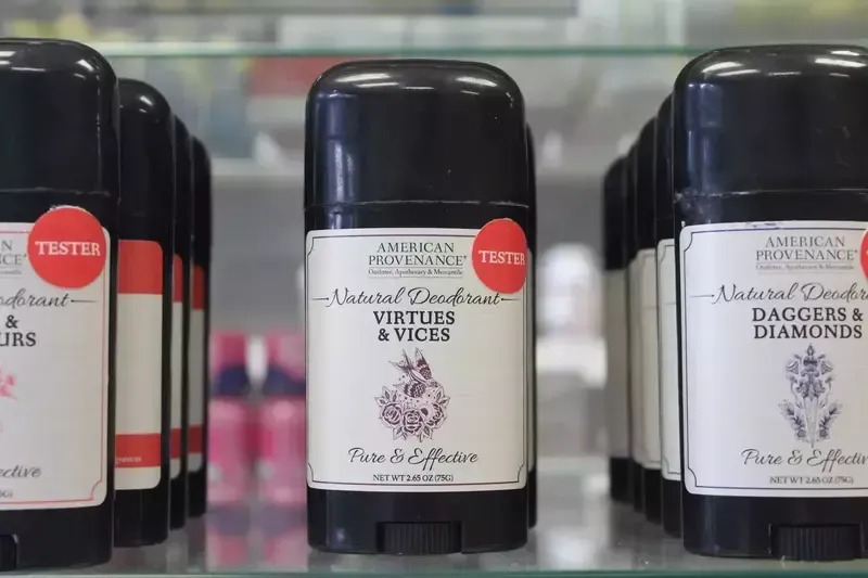 Three bottles of deodorant are lined up on a glass shelf.