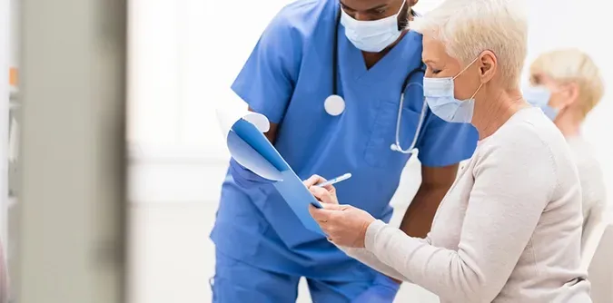 A nurse is talking to an elderly woman wearing a mask in a hospital.